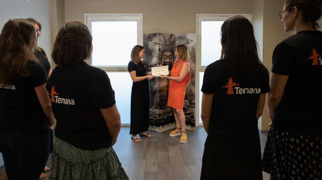 À la fin d'une formation massage reconnue par l'état, une formatrice remet son certificat à une stagiaire devant le groupe en tee-shirt TEMANA