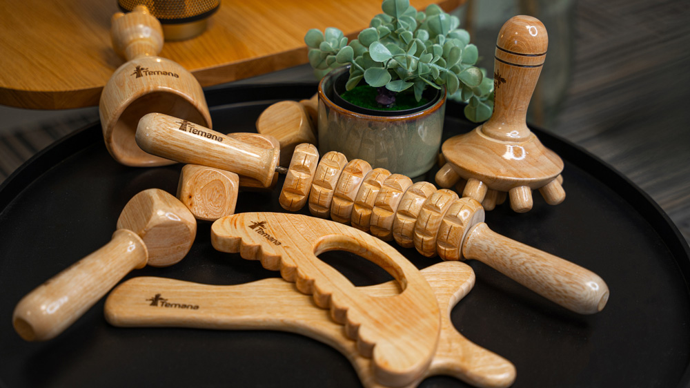 Les outils de madérothérapie gravés TEMANA posés sur un plateau noir : coupe, rouleau à picots, cubes, champignon et planches en bois