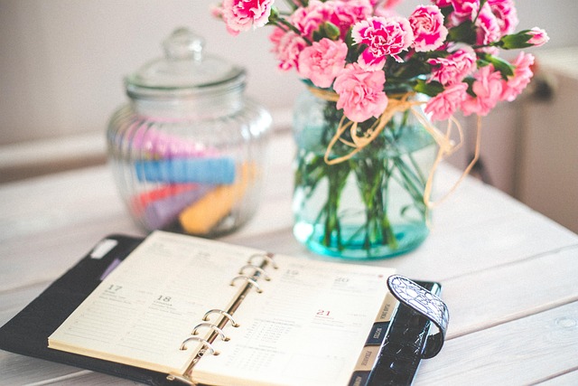 Agenda ouvert sur une table blanche, à côté d'un bouquet d'œillets roses et d'un bocal de surligneurs