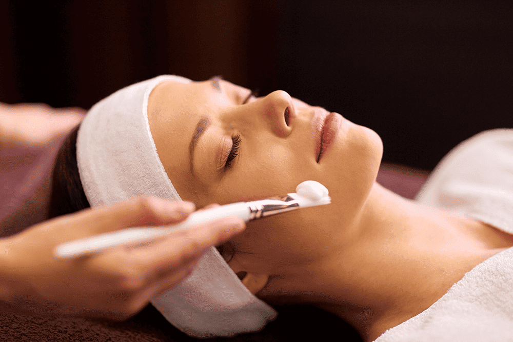 Esthéticienne appliquant un masque facial à une cliente dans un spa.
