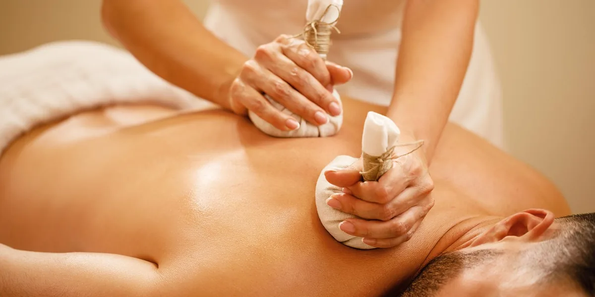 Une praticienne applique deux compresses de plantes chaudes sur le dos d’un massé, un protocole enseigné en école de massage