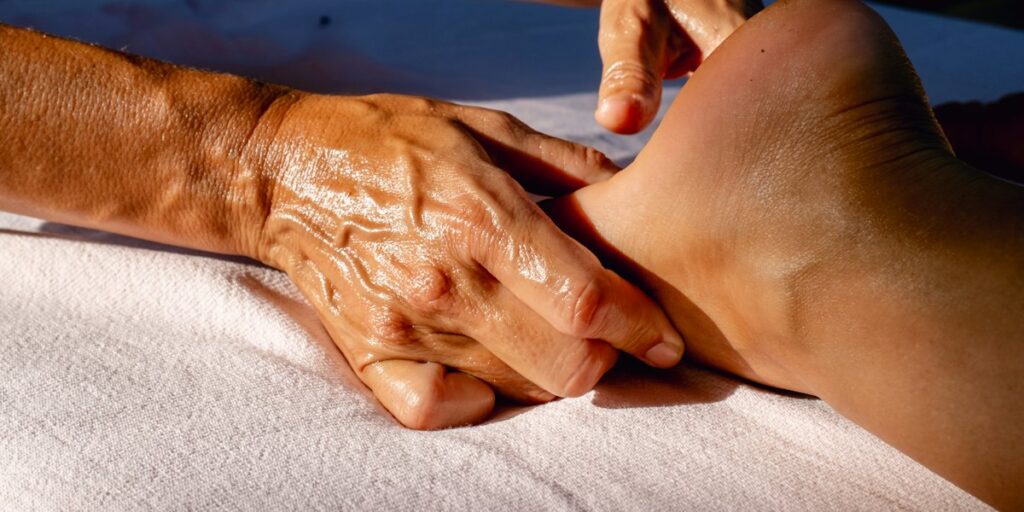 Deux mains huilées saisissent et compriment un mollet en pleine lumière, le pétrissage de la technique du massage suédois