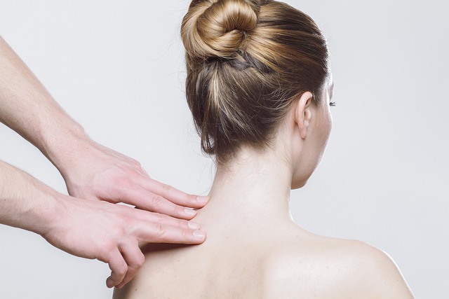 Deux mains posées sur le haut de l'épaule d'une femme vue de dos, cheveux attachés en chignon, sur fond blanc