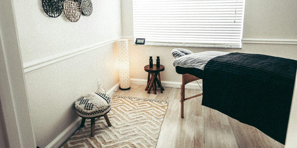 Une table de massage pliante en bois installée dans une pièce dédiée, avec lampe, tapis et tabouret