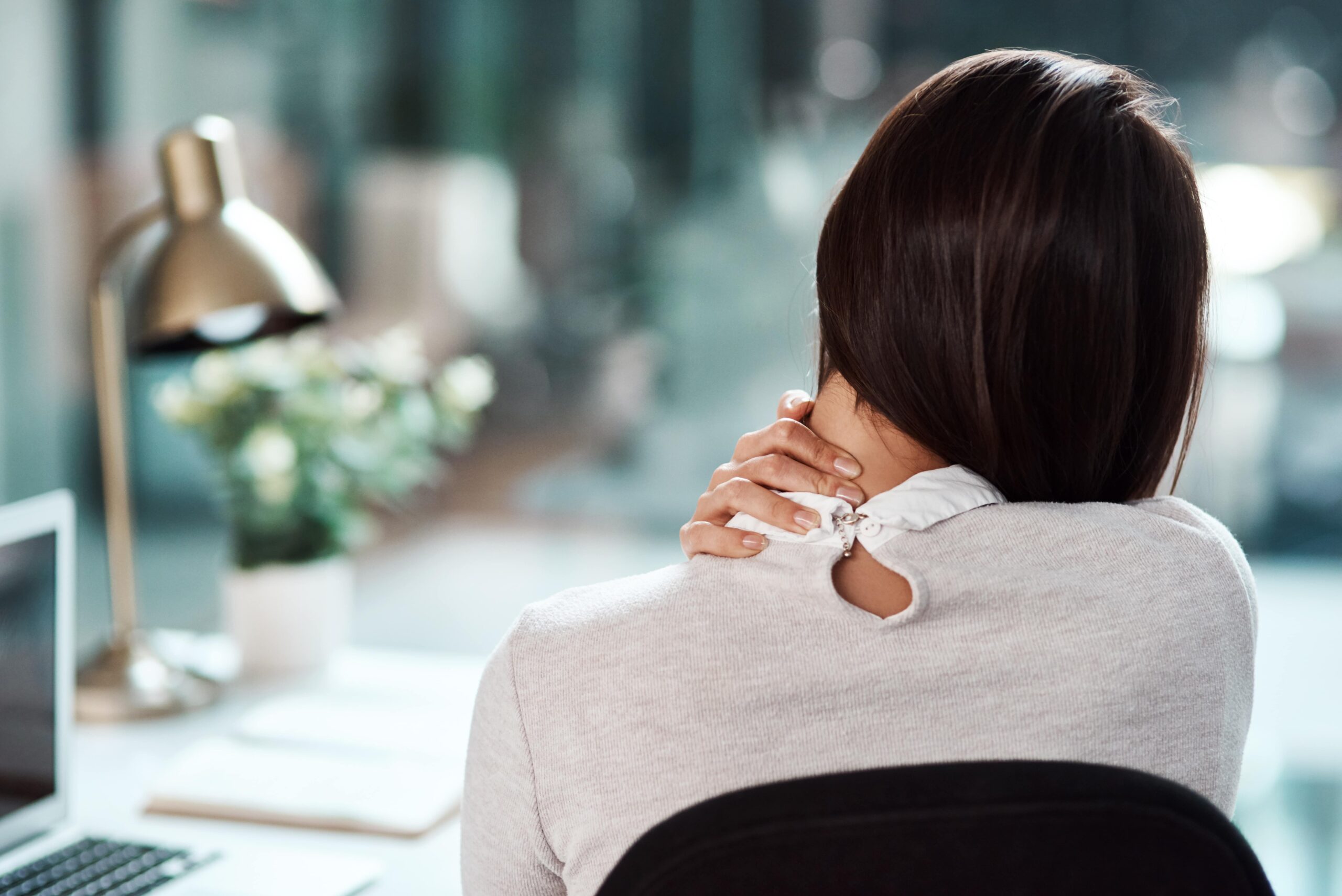 Après un massage douloureux, une femme assise à son bureau se tient la nuque d'une main